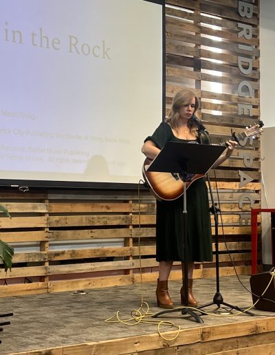 Woman in black dress holding a guitar singing songs at women at the well event